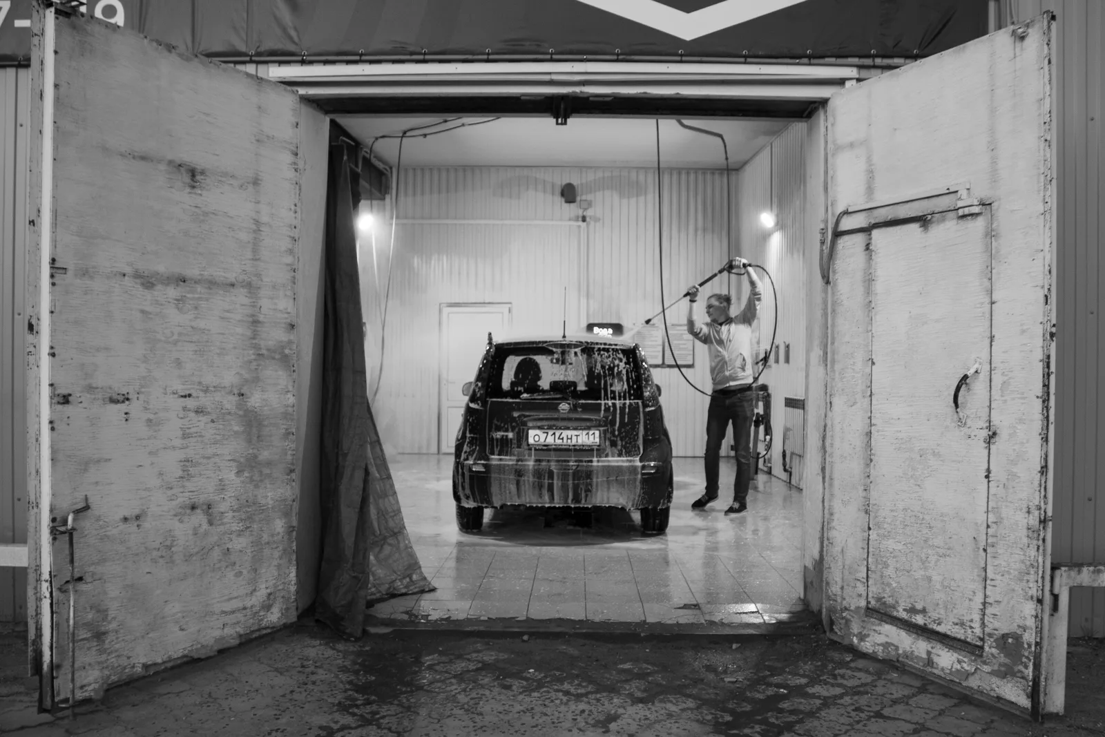 Black and white image of a man washing a car in a garage setting. Which car wash locations actually justify the rent?
