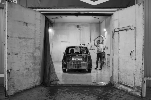 Black and white image of a man washing a car in a garage setting. Which car wash locations actually justify the rent?