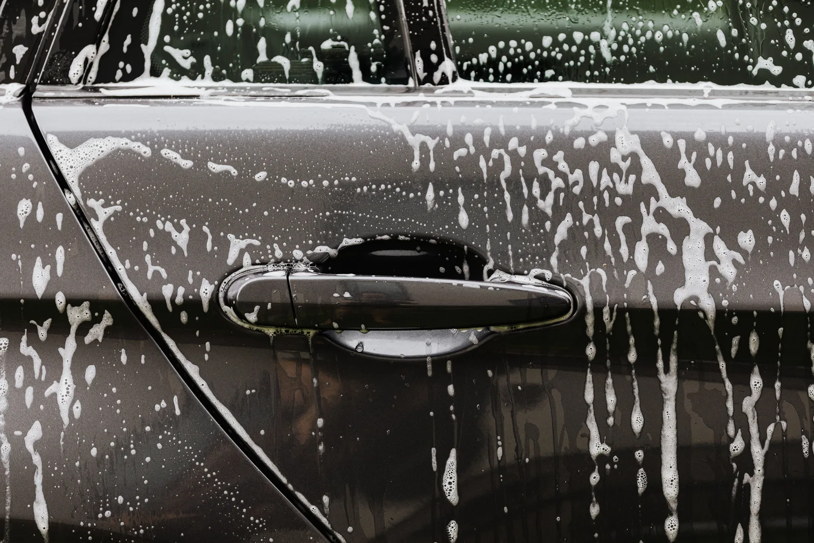 Detailed close-up of soap suds on a black car door during a wash, highlighting automotive care. Car wash cash flow: the basics, the traps and the fixes