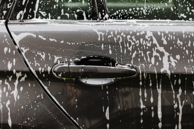 Detailed close-up of soap suds on a black car door during a wash, highlighting automotive care. Car wash cash flow: the basics, the traps and the fixes