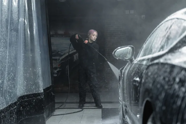 A young woman in a black outfit washing a car with foam and water spray indoors. Car Wash Winter Throughput: Keeping Bays Open in Alberta