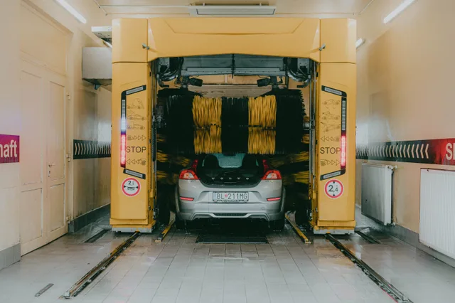 A car undergoing a cleaning process in an automated car wash station with a yellow gantry machine. How to Increase Car Wash Bay Throughput Without Adding Equipment
